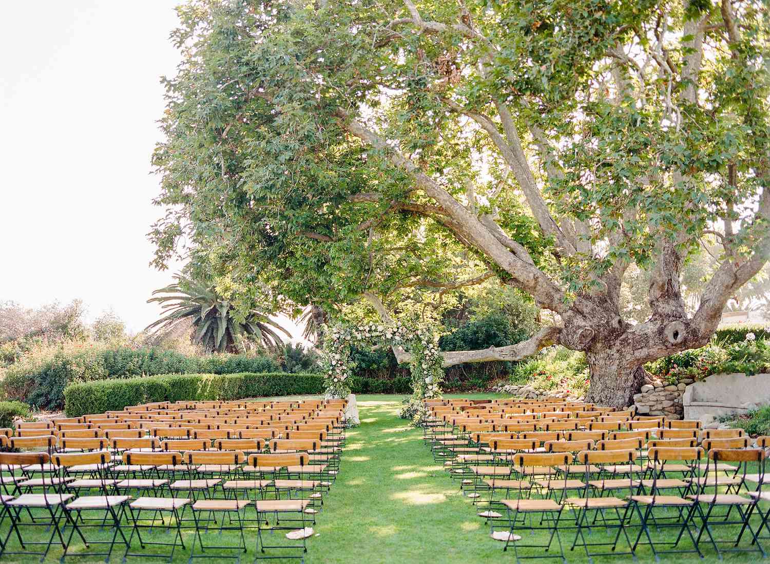Backyard wedding aisle with rows of empty chairs and a greenery and floral arch