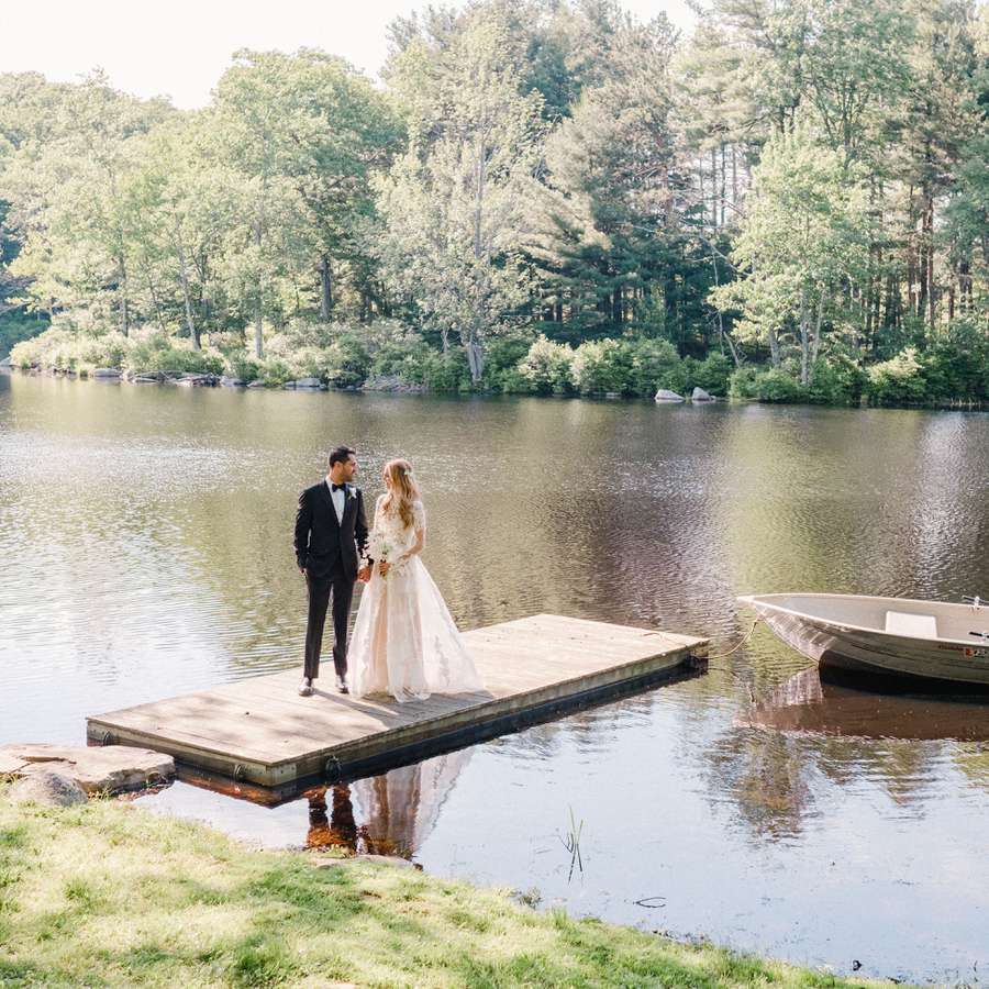 A bride and groom standing on a dock at their summer camp wedding.