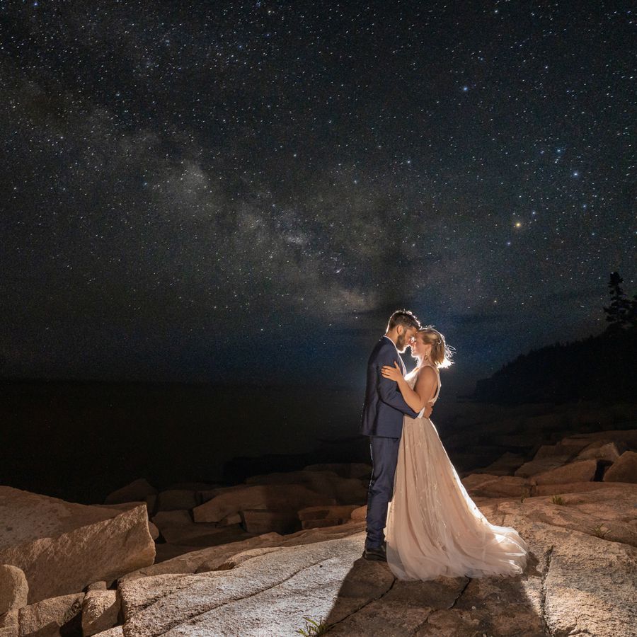Bride and groom embrace under the stars on a cliff in Maine