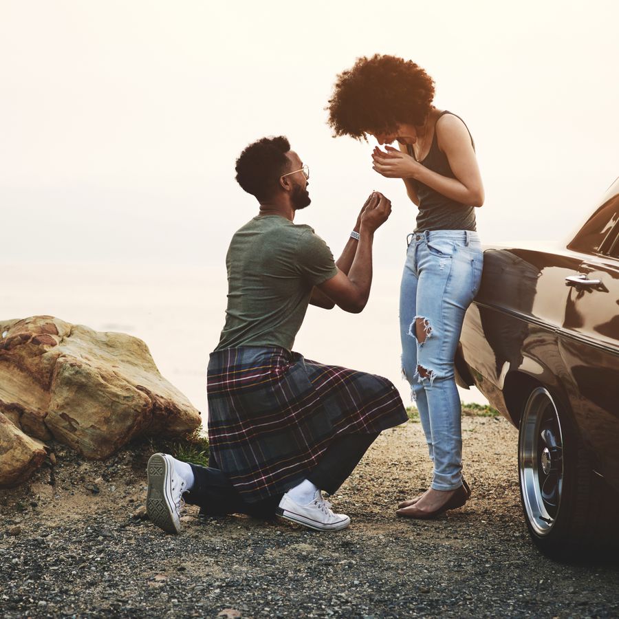 A man proposing to his girlfriend on a rocky terrain near their car