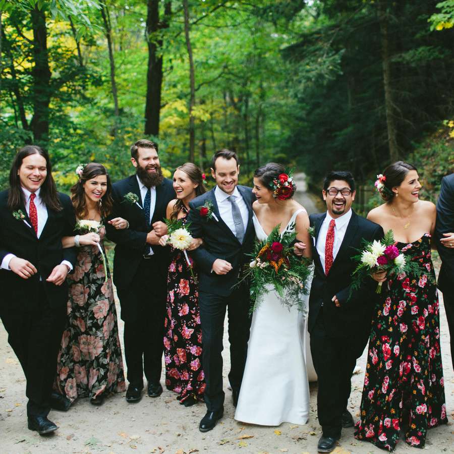 Bridesmaids in floral dresses outdoors with groomsmen, bride, and groom