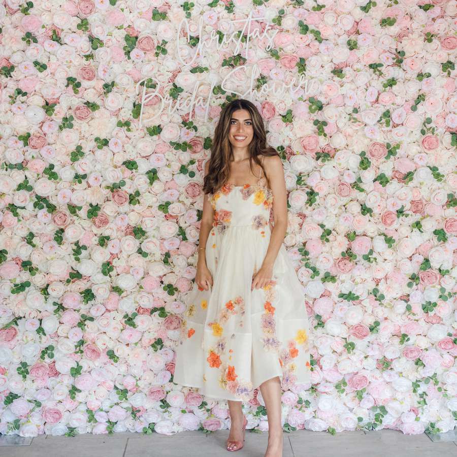 Bride in a floral dress standing in front of a flower wall with a neon sign