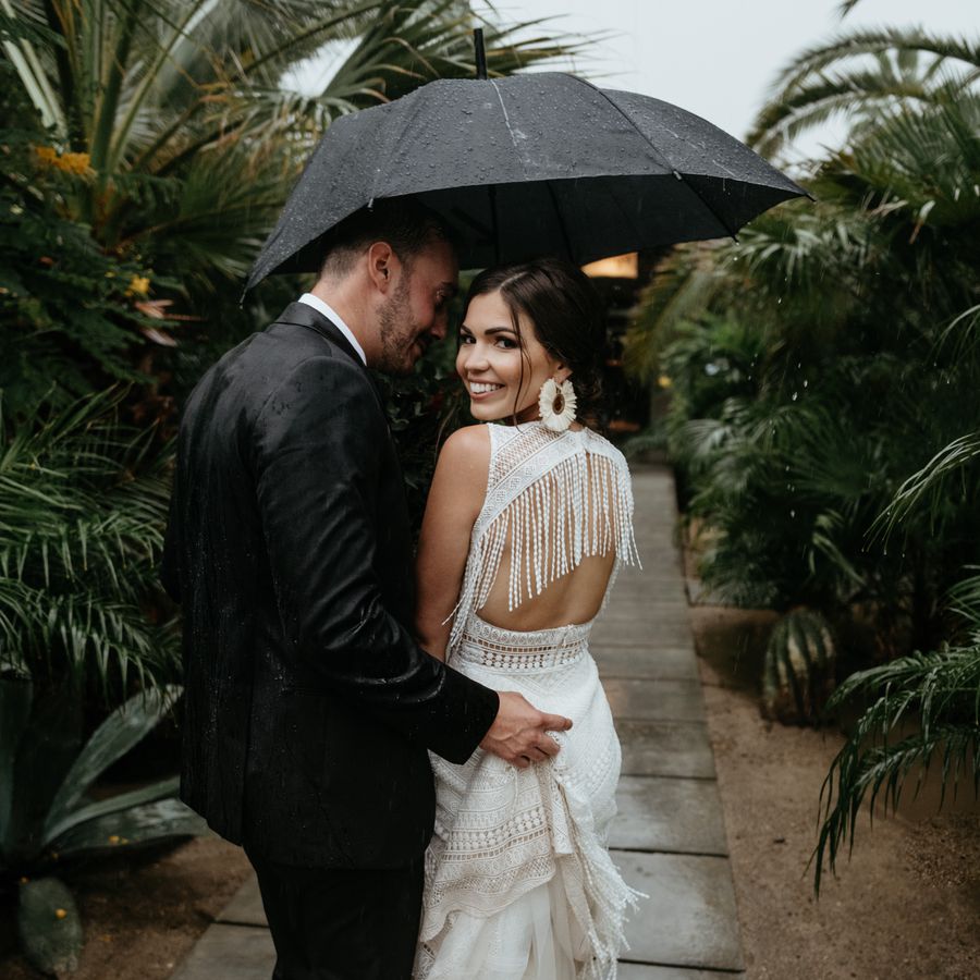 Bride and groom stand together under umbrella