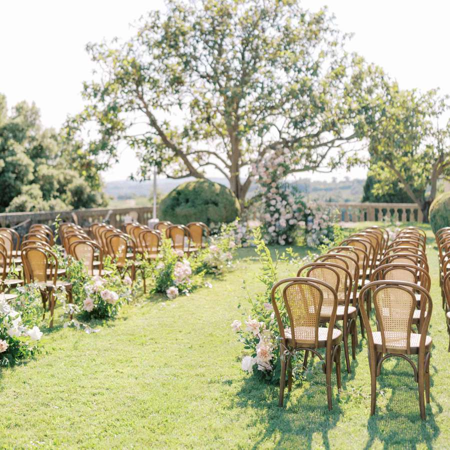 Wedding ceremony design with cane chairs and pink and green floral arrangements along the aisle