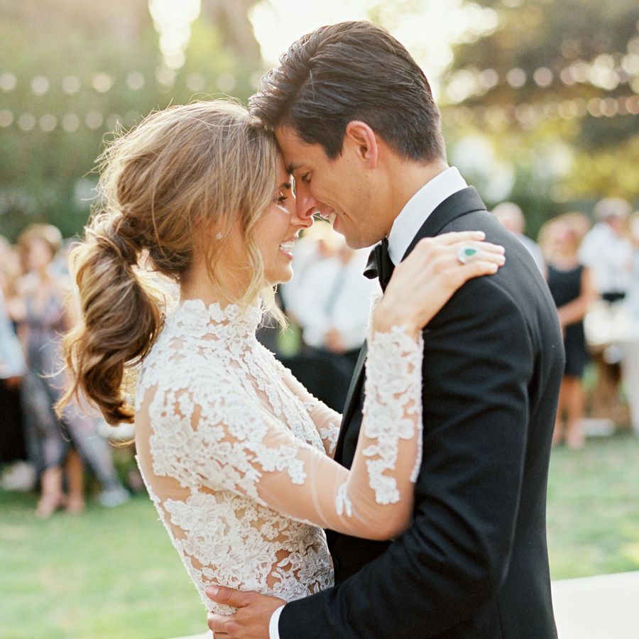 bride with ponytail and groom holding each other with foreheads touching during their first dance