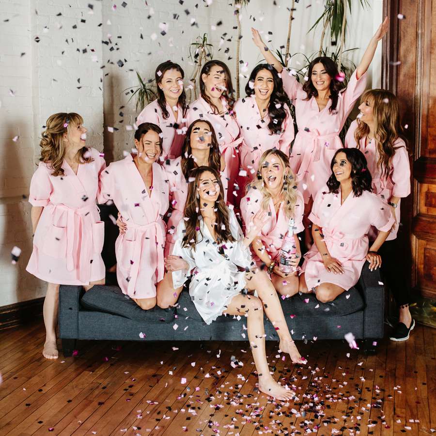 women in pink and white robes at bachelorette party throwing confetti in the air