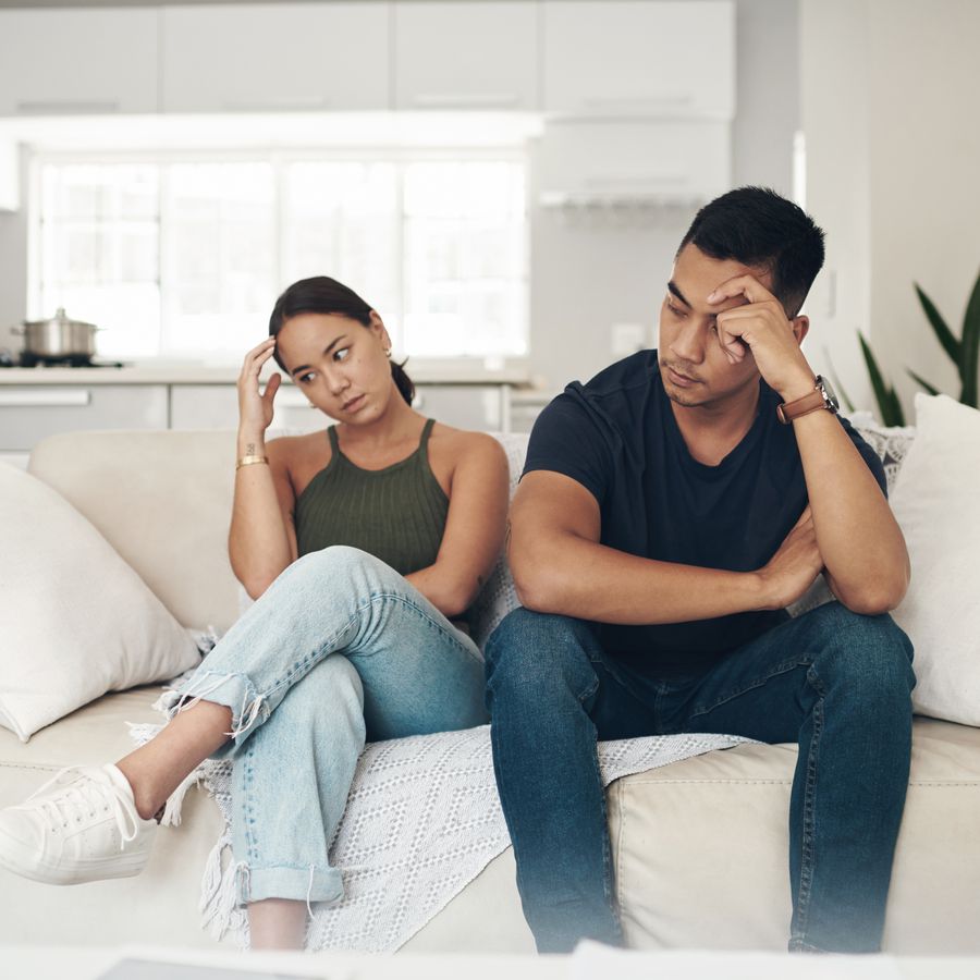 young couple sitting on a couch looking frustrated 