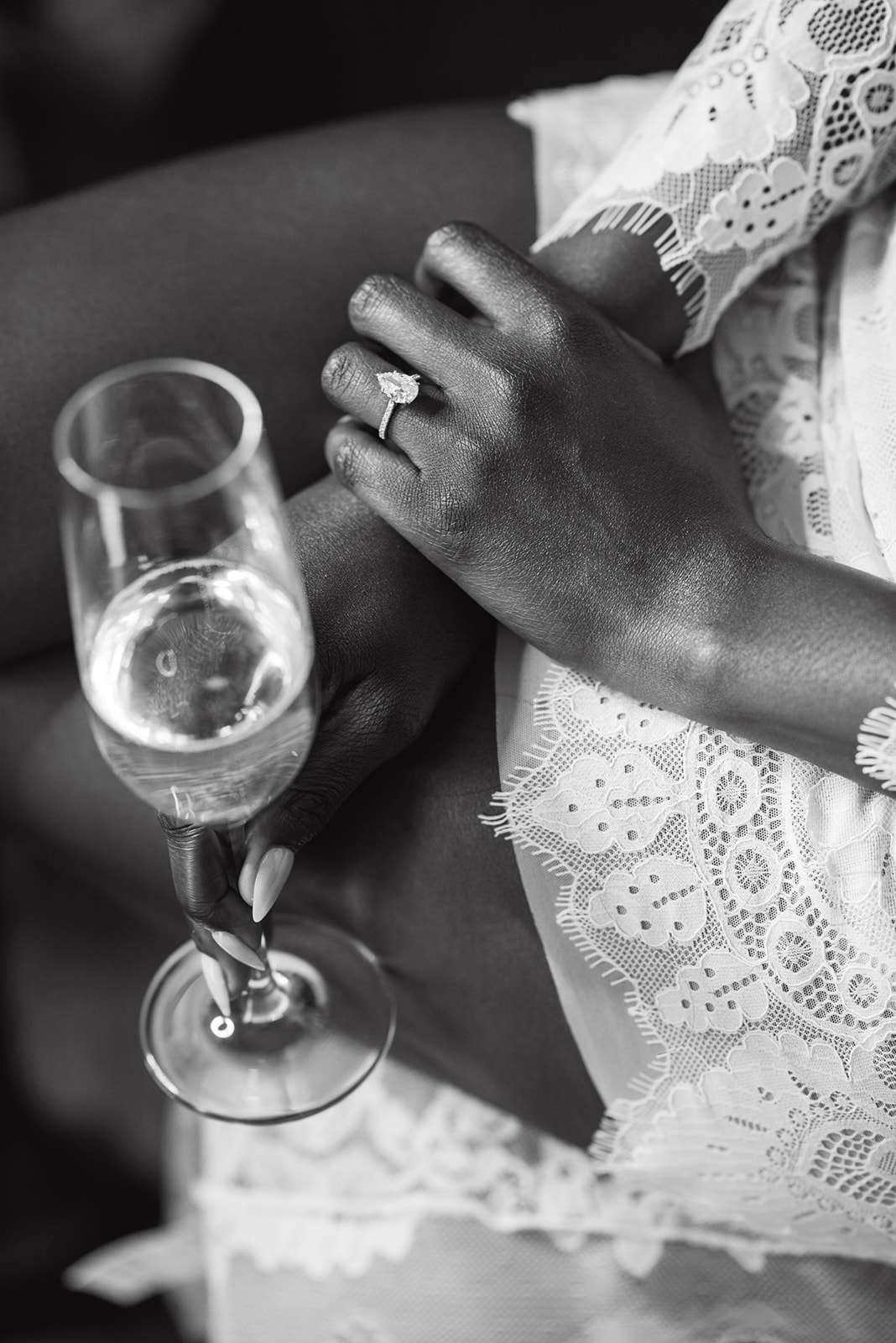 Bride's hand wearing pear-cut engagement ring holding a glass of champagne