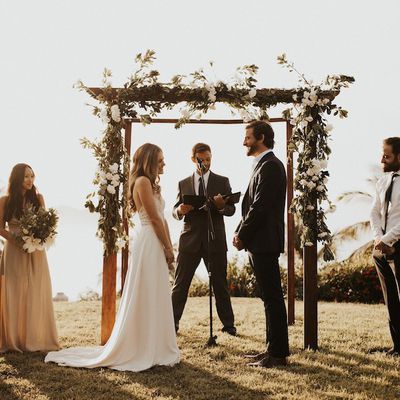 Bride and groom at altar in front of a wooden arch covered in white flowers, exchanging vows