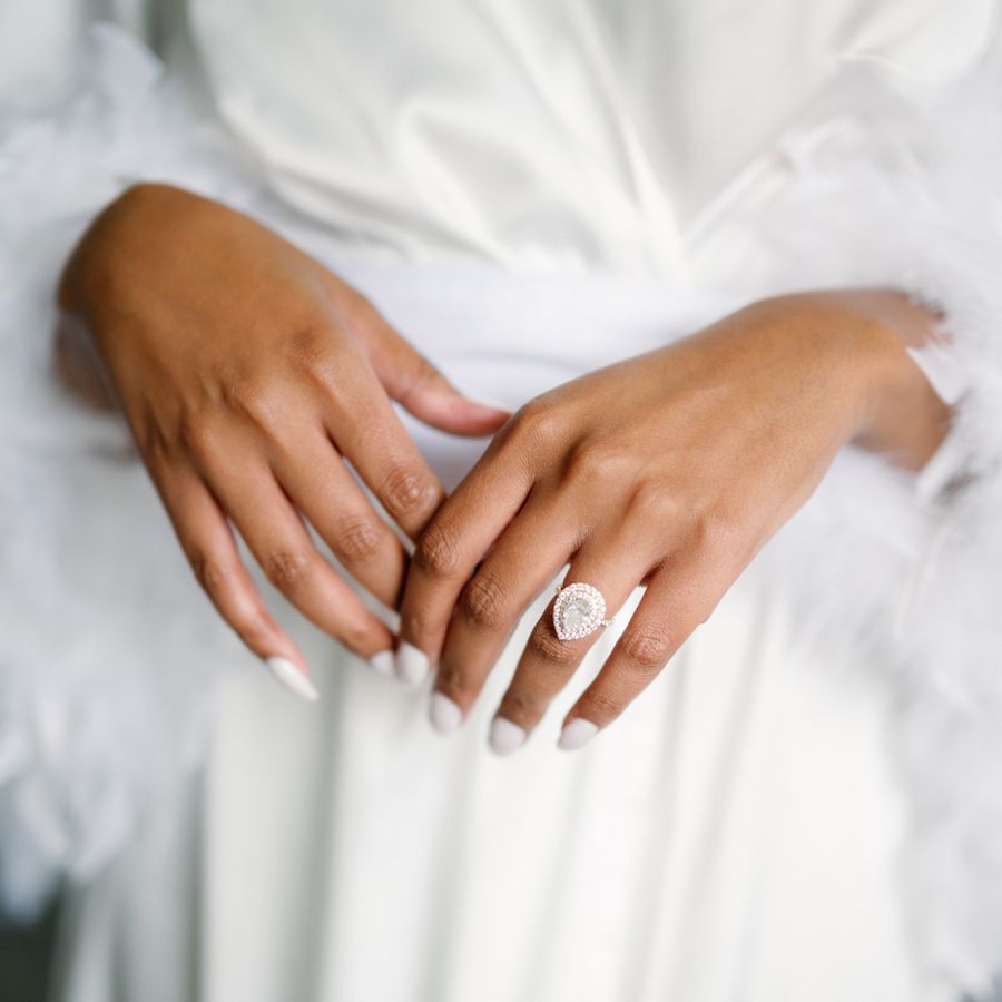 a pair of hands with white nail polish and a pear-shaped engagement ring