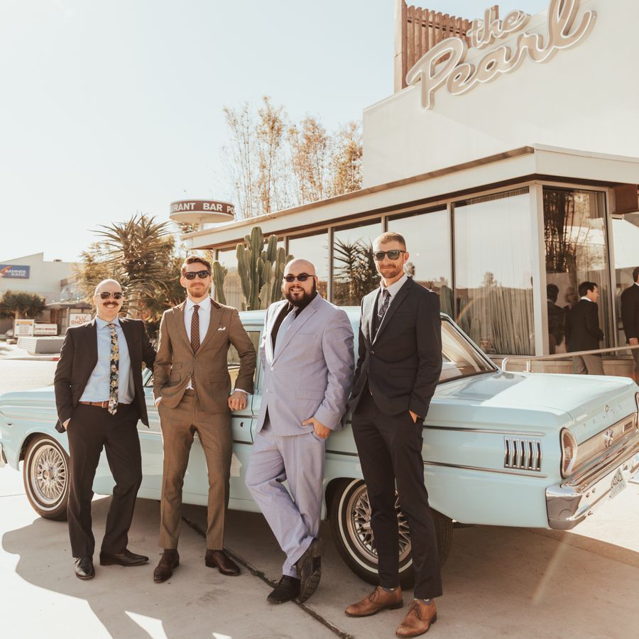 four men in suits standing next to vintage car