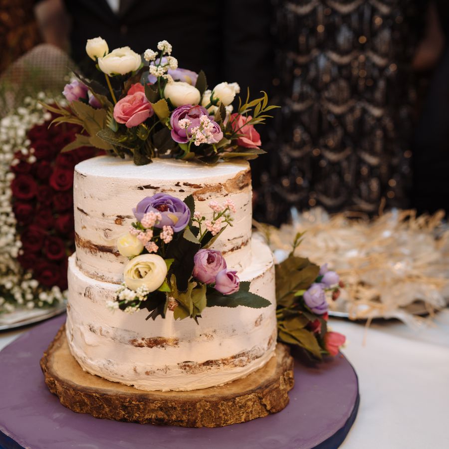Two tier semi-naked cake with pink, purple and white flowers on purple stand