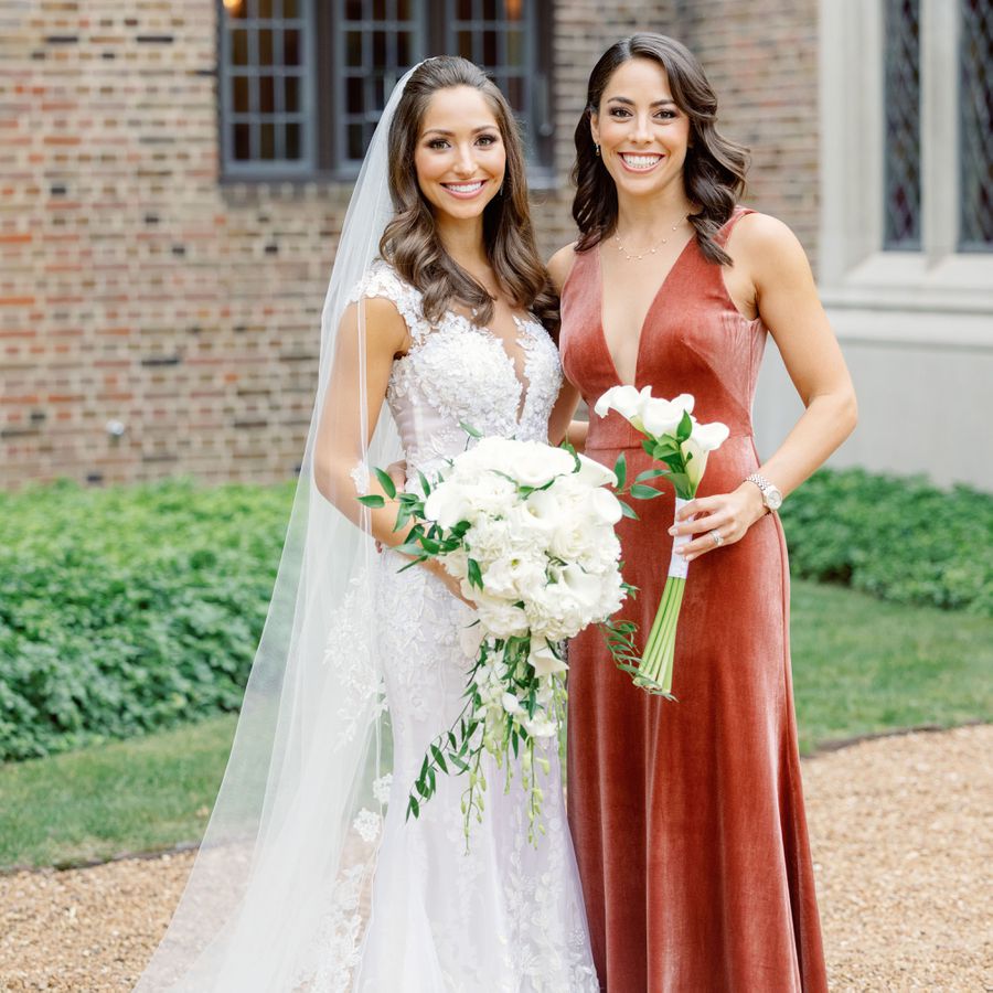 A bride holding a white bridal bouquet with roses and calla lilies next to her bridesmaid with a simple calla lily bouquet.