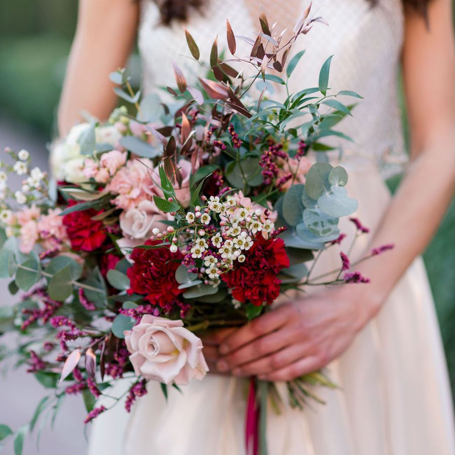 A wedding bouquet of red carnations, eucalyptus, and pink roses.