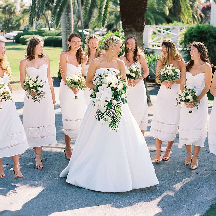 Bride smiling and looking back at her bridesmaids in white tea-length dresses outdoors