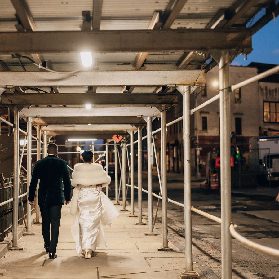 A bride and groom in formal attire walk on the sidewalk in Brooklyn during their city wedding.