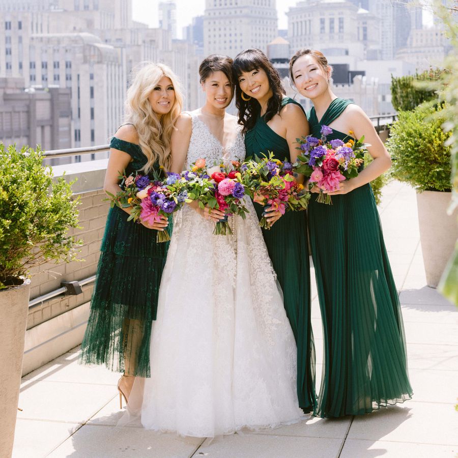 Bride standing on city balcony with 3 bridesmaids in sleeveless emerald green gowns