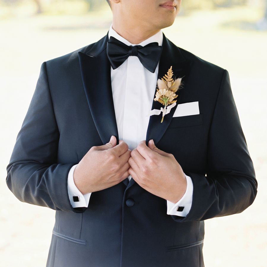 close up shot of a groom in a tuxedo, bowtie, and a dried grass boutonniere