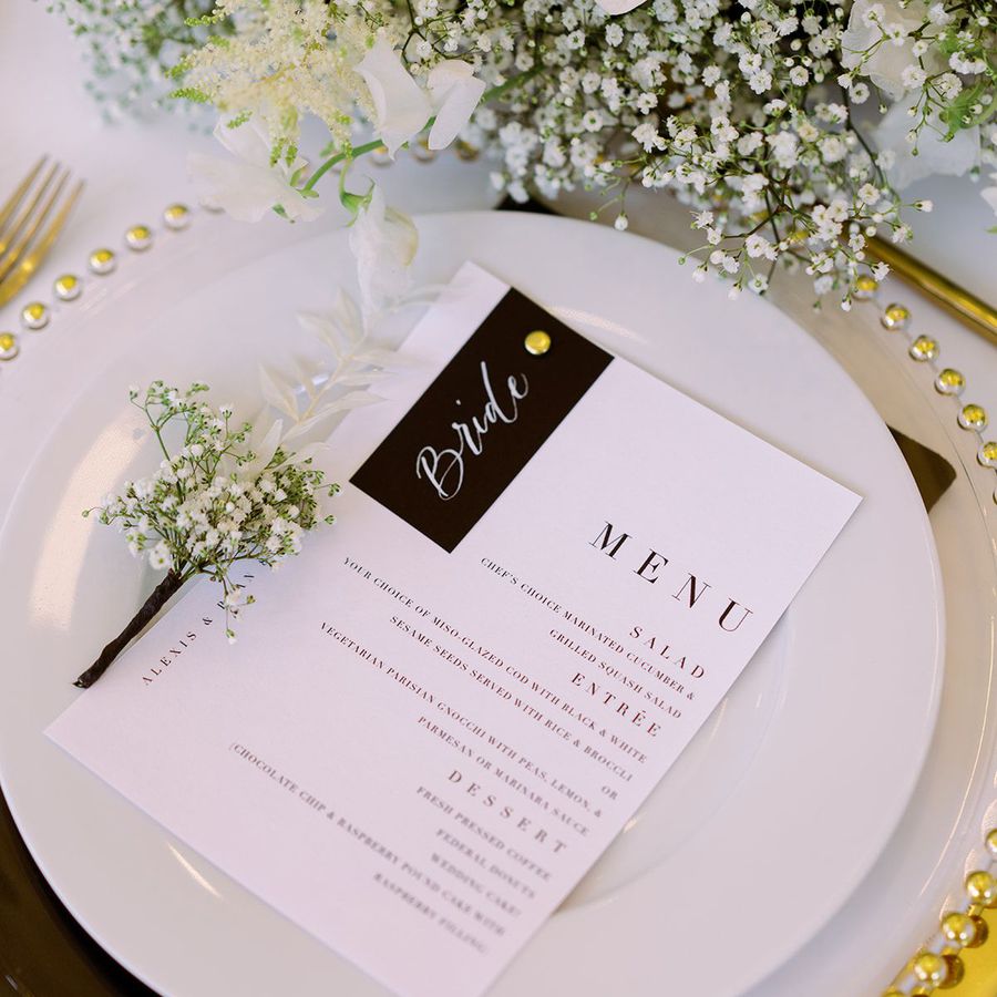 table setting with white plate, gold charger, black and white menu, baby's breath on plate, and baby's breath flower arrangement