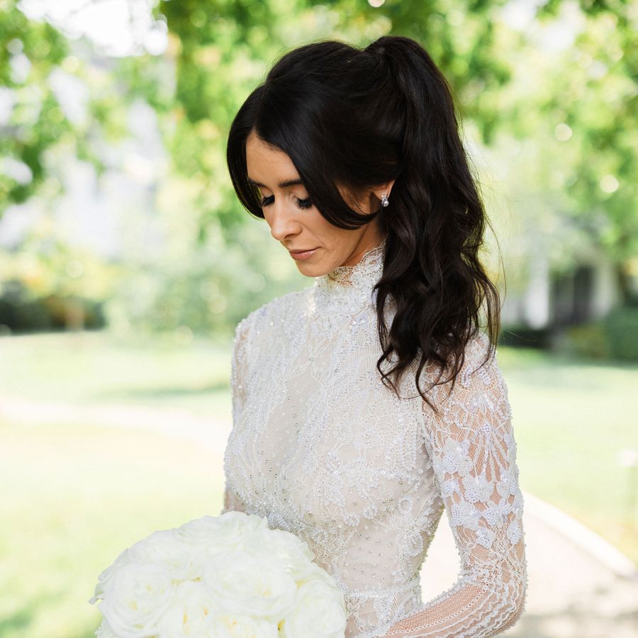 A bride in a long-sleeved embellished mock neck with her hair in a wavy high ponytail with curtain bangs