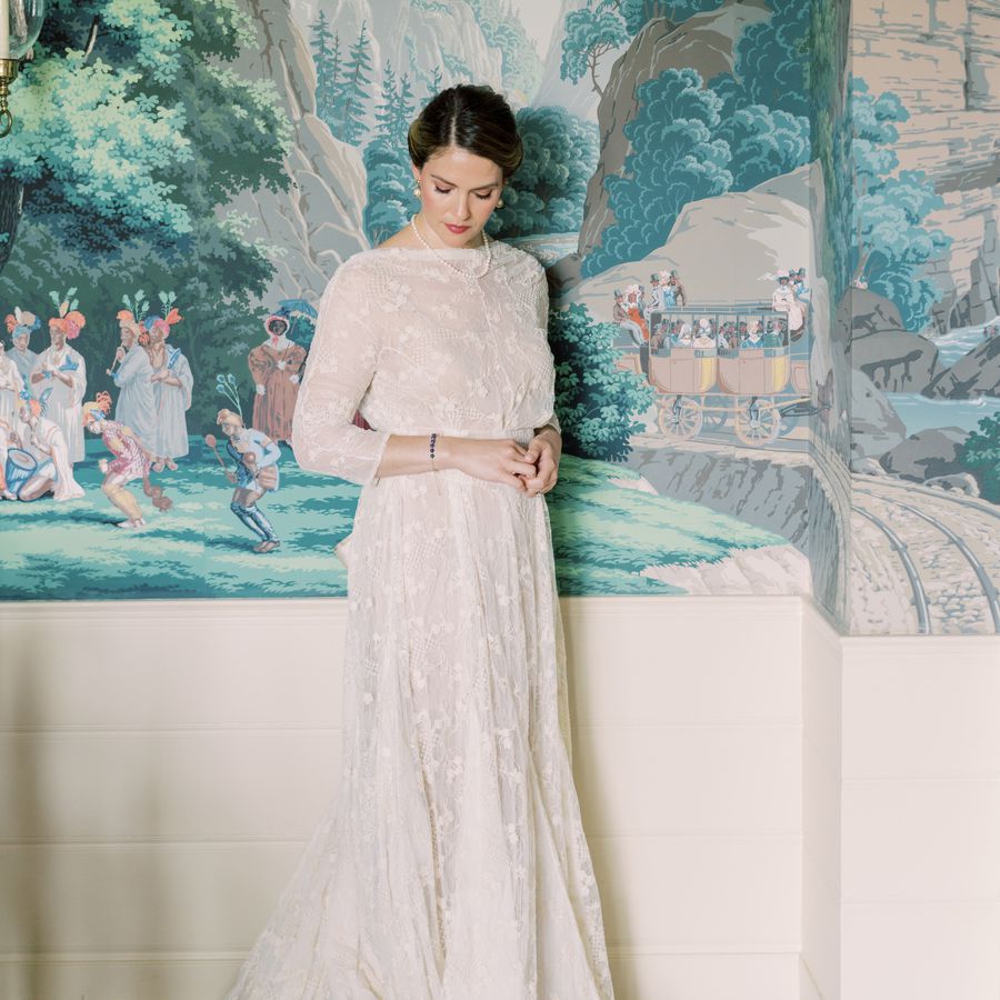 Bride looking down in a long-sleeved lace wedding dress, pearl earrings, and a pearl necklace