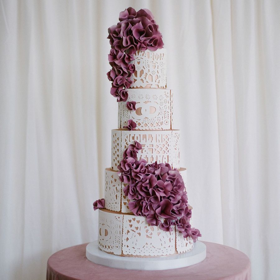 Five-tier white lace wedding cake with purple sugar flowers cascading down the design