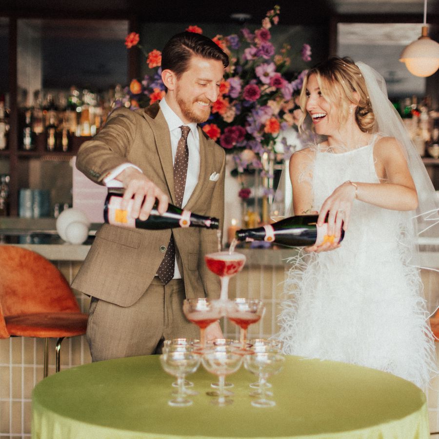 A bride and group pouring rose champagne over a champagne tower as an alternative to the first dance during their indoor wedding reception. 