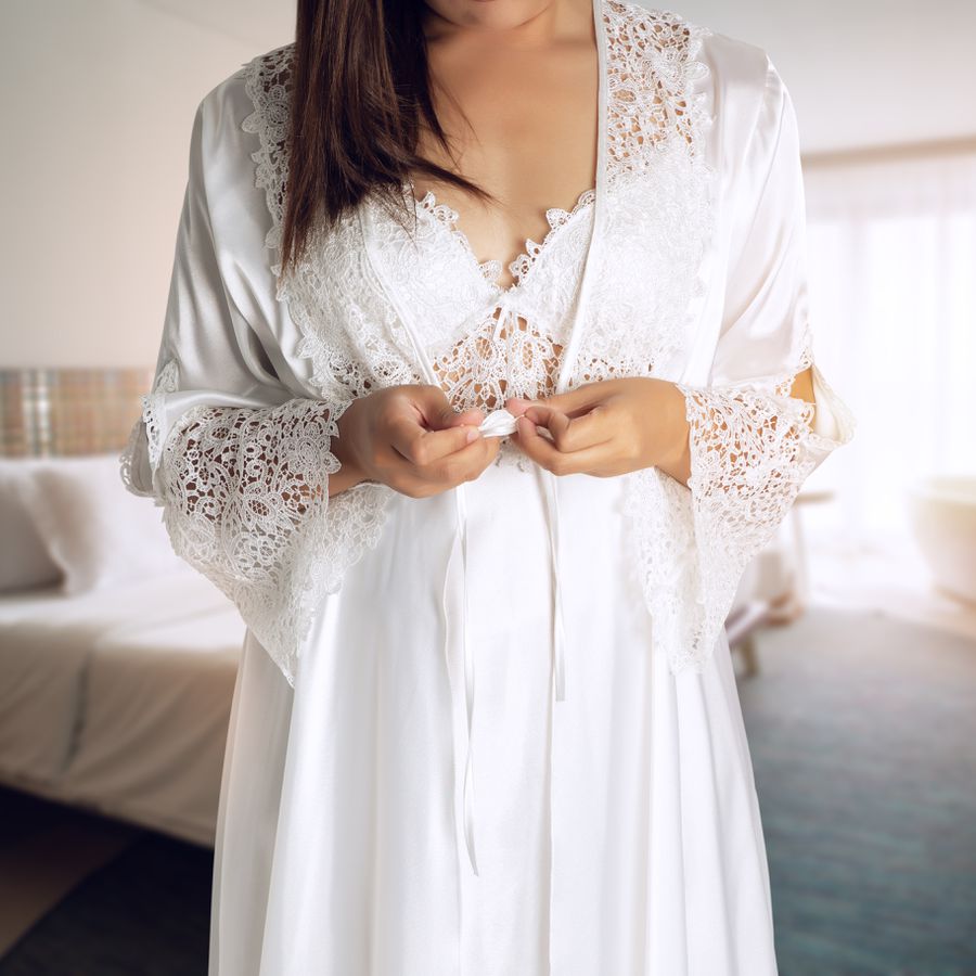 Woman holding the ties of a white robe made of satin and lace