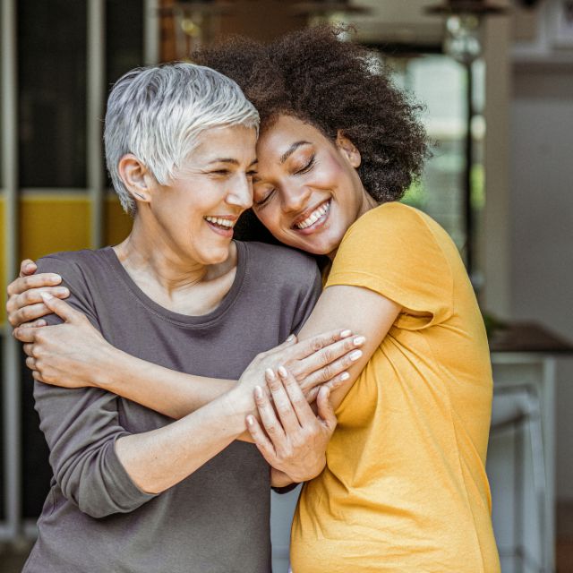 Young woman hugging older woman, both are smiling