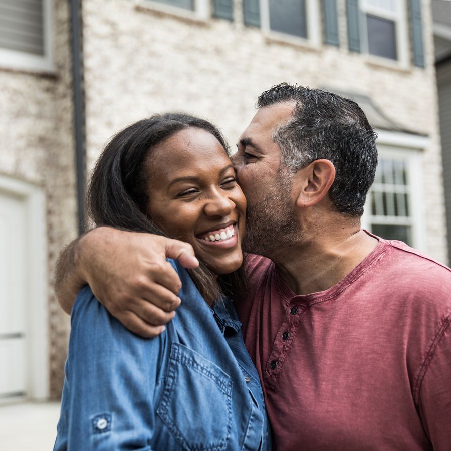Man kissing a woman on the cheek in front of a house