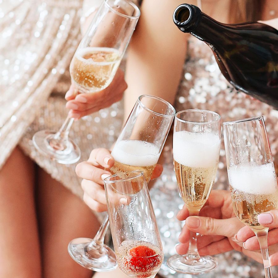 Women in sparkly dresses pour champagne into champagne flutes with strawberries at a bachelorette party.