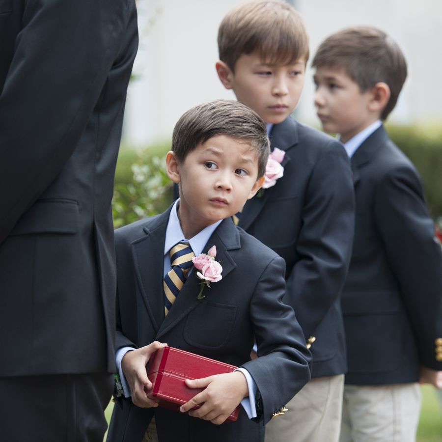 Ring bearer holding red wedding ring box at outdoor wedding ceremony with nearby wedding party members