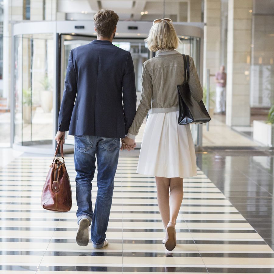 Couple holding hands and carrying leather bags as they walk through a lobby