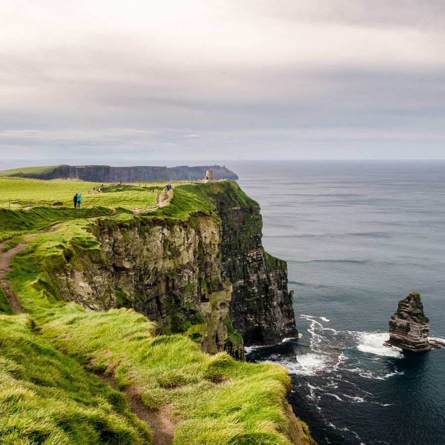 A couple walking along the vibrant green Cliffs of Moher in Ireland on a cloudy day.