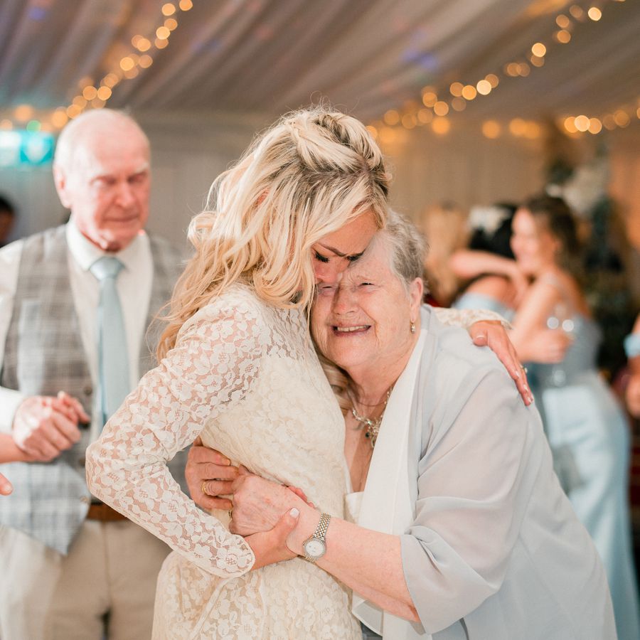 Bride in long-sleeved lace wedding dress hugging her grandmother