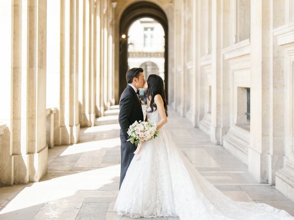 Groom in Black Tuxedo Kissing Bride in Strapless Ball Gown Wedding Dress in Paris Archway Wedding Venue