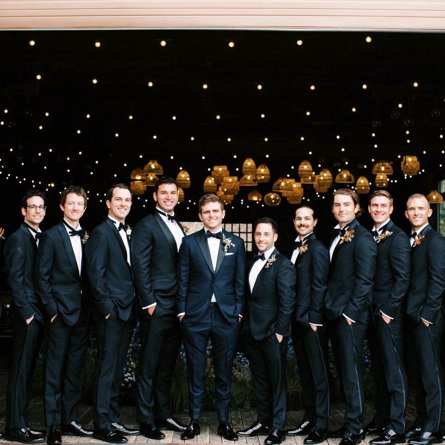 Groomsmen and a groom in black tuxedos at a wedding.