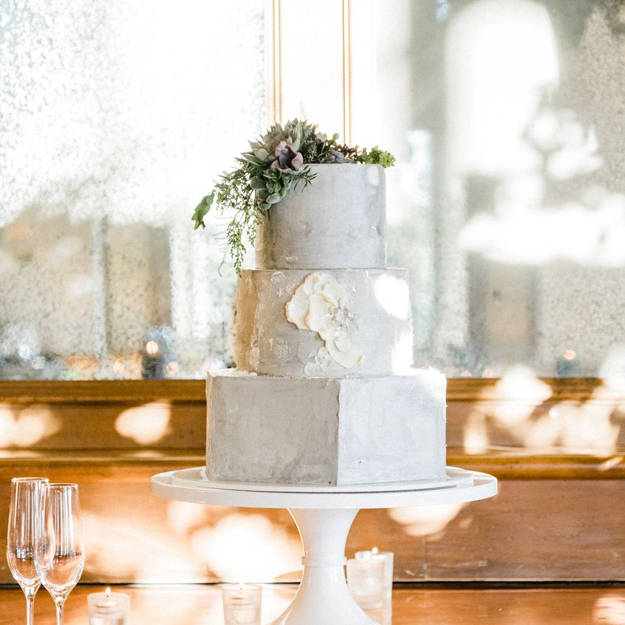 A three-tier off-white wedding cake with a hexagon base tier and greenery on top.