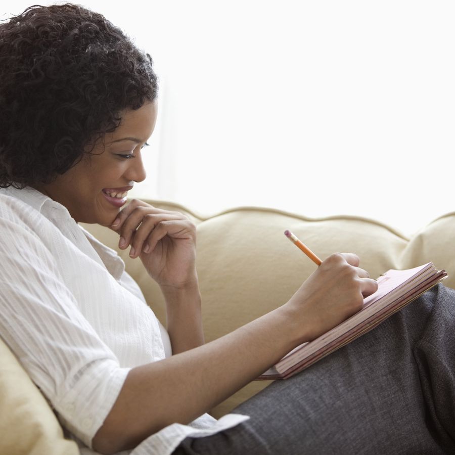 A woman sits on the couch writing a letter.