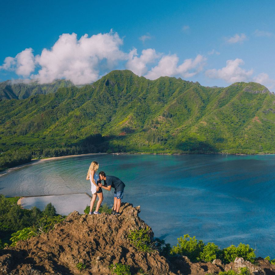 A man kissing the belly of a pregnant woman on a mountain in Oahu