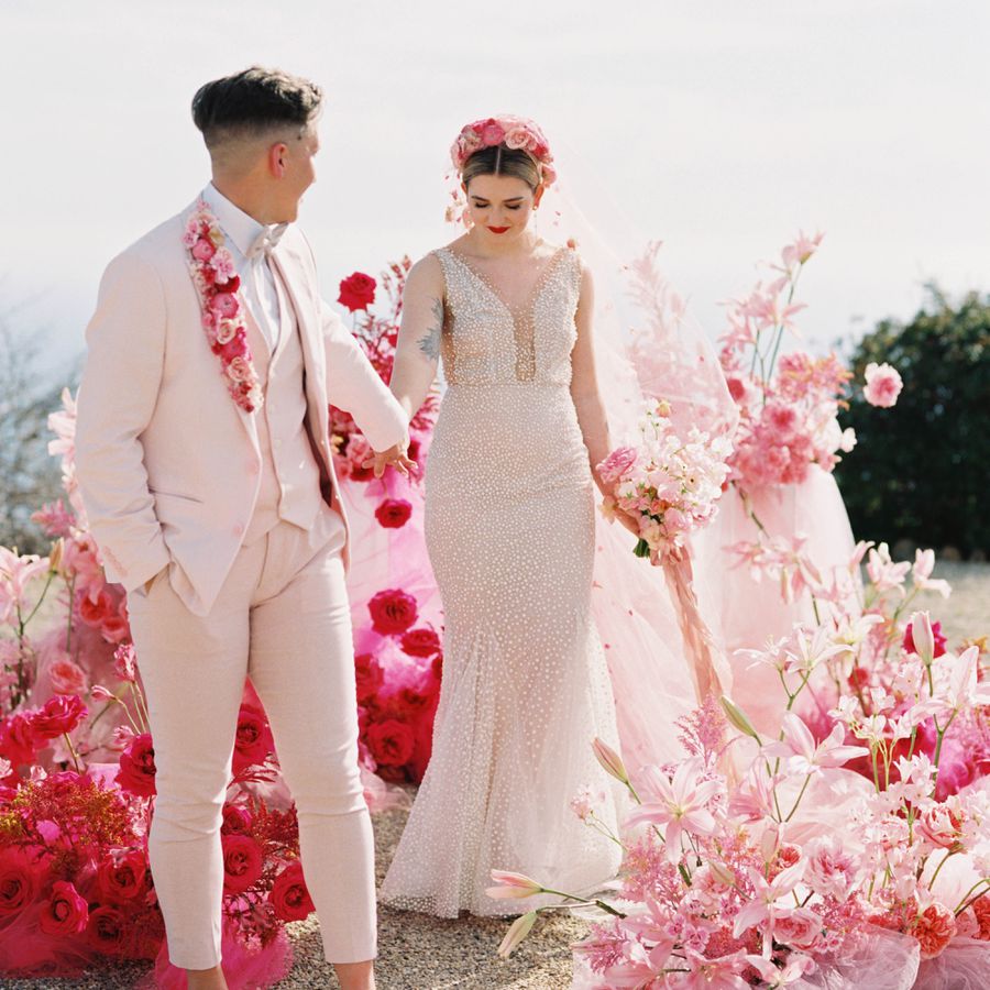 Brides Holding Hands with Pink Floral Ceremony Backdrop Behind Them