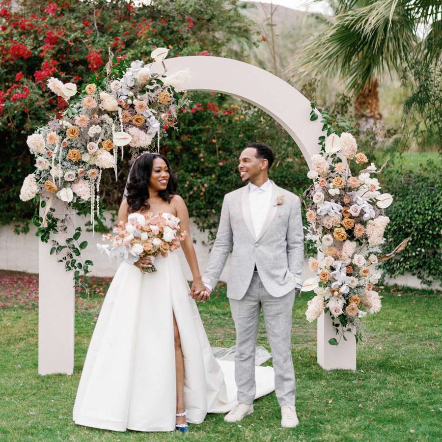 Bride and groom holding hands in front of a semicircular floral arch