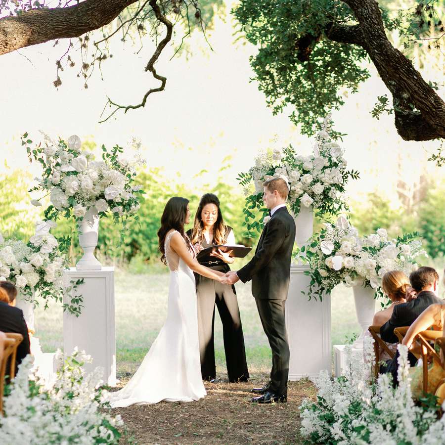Outdoor wedding ceremony with a wedding officiant, white flowers on a sunny day.