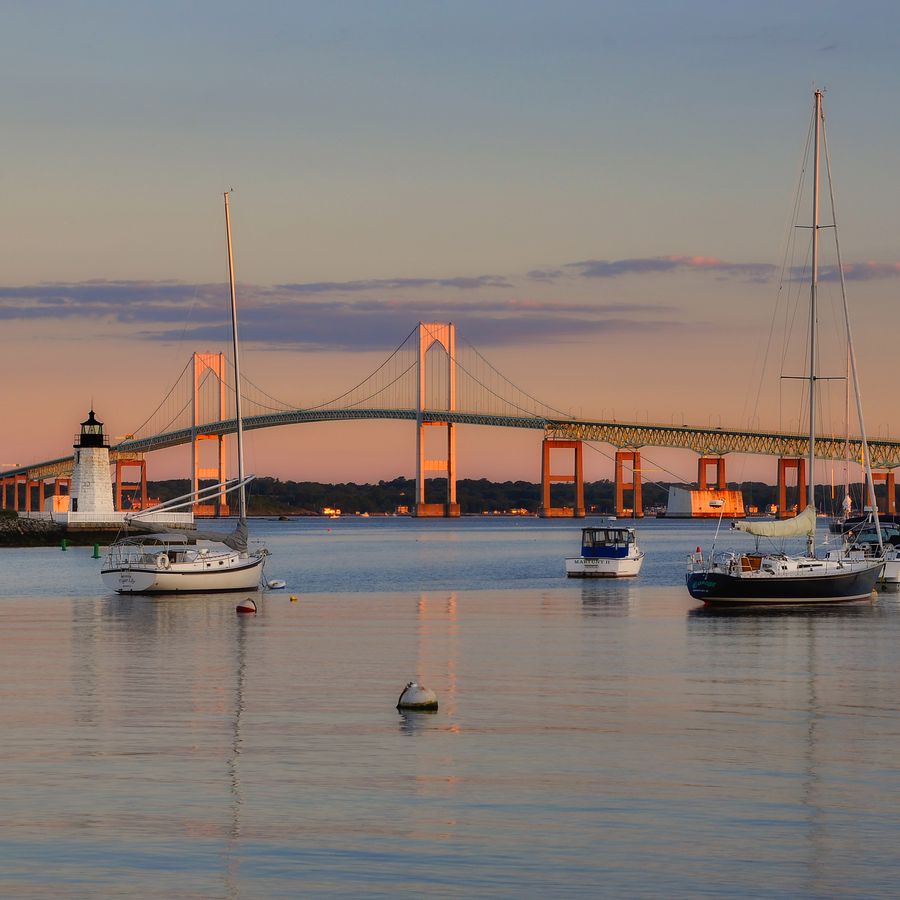 Newport, Rhode Island bridge at sunset with sailboats and lighthouse in the harbor