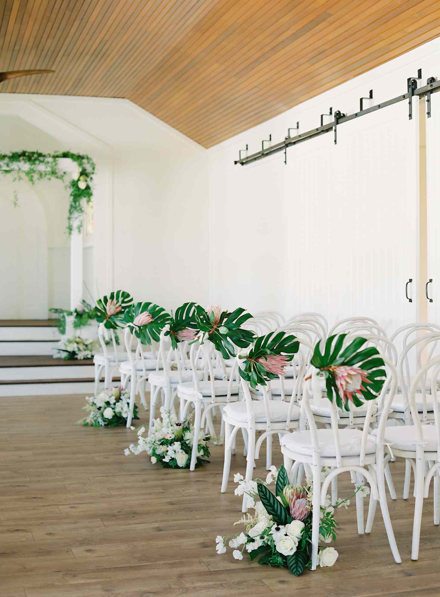 Ceremony aisle with monstera leaf and protea arrangements on chairs