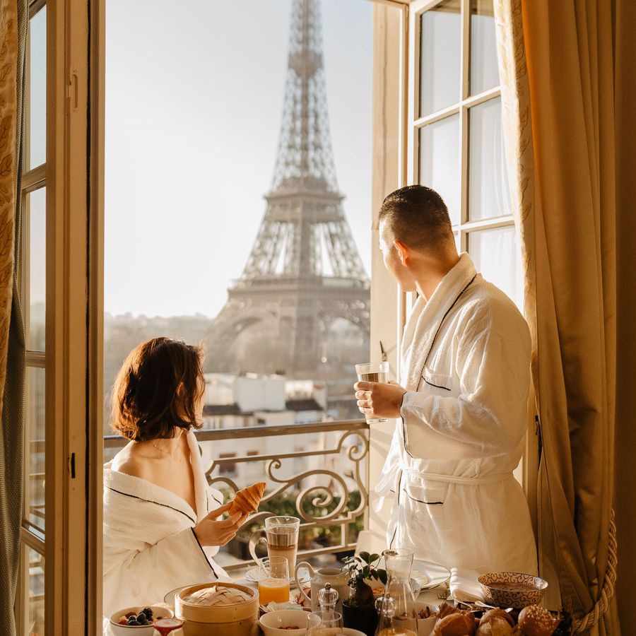 A couple looks at the Eiffel Tower from their hotel during their Paris honeymoon.