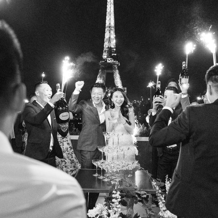 bride, groom, and wedding guests cheering with champagne and sparklers in front of the eiffel tower