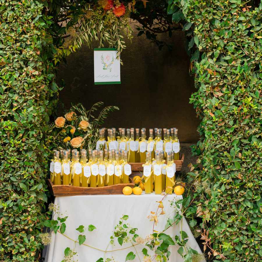 Bottles of limoncello affixed with custom labels presented on a table covered in white linens and framed by boxwood