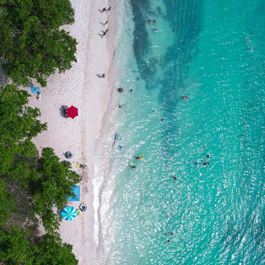An aerial shot of the white-sand beach in Puerto Rico with bright blue water on a sunny day. 
