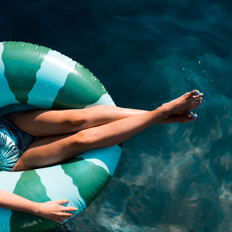 Woman in a green and white swimming tube laying in a pool with outstretched, tan legs.